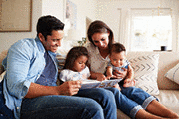 Young family of four sitting on the sofa reading a book together.