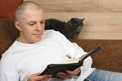 A man sitting on a sofa and reading a book of the Bible.