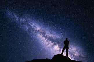 Landscape with purple Milky Way with a silhouette of a man on the stone.